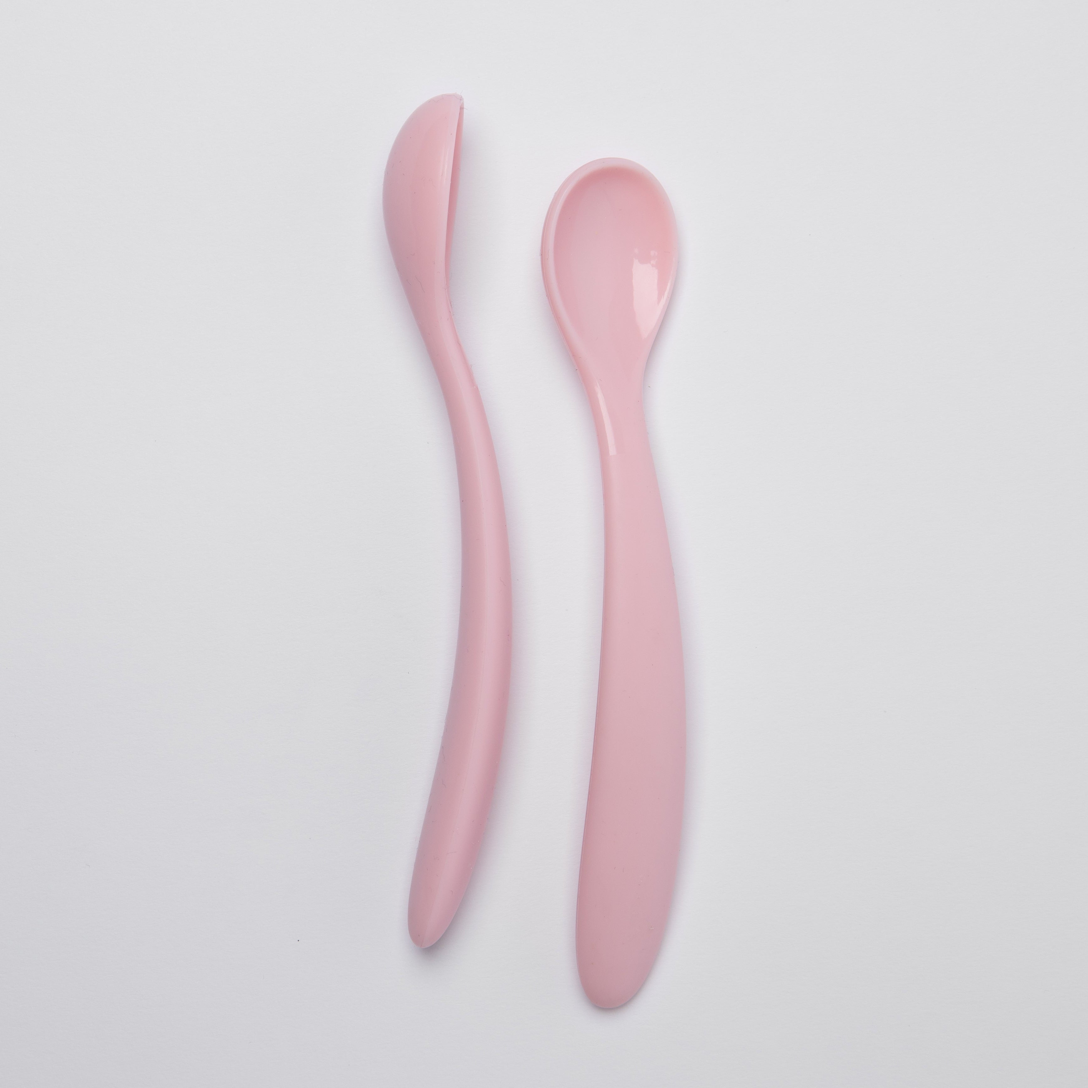 Two pink ceramic spoons on a light gray background