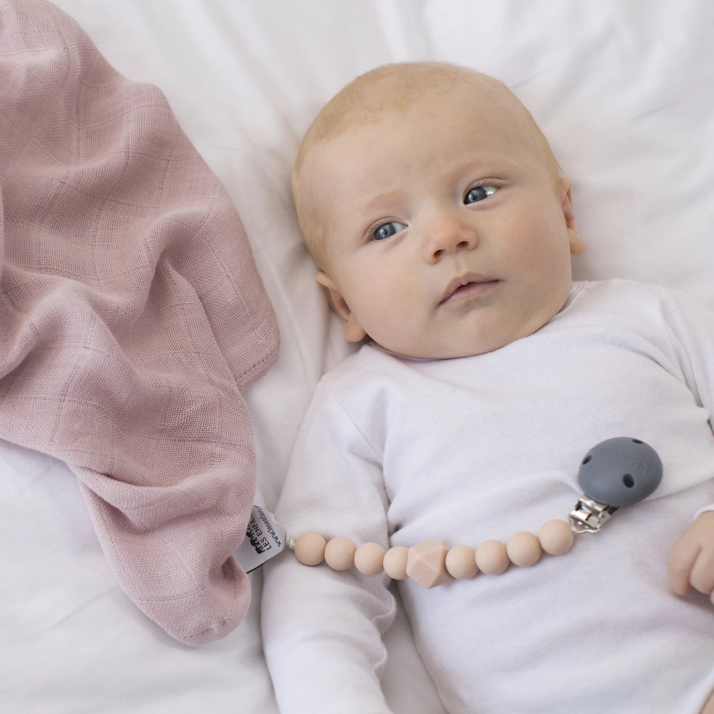 The Les Enfants Chewy Pacifier Clip pink with blond model and pink 100% bamboo muslin blanket