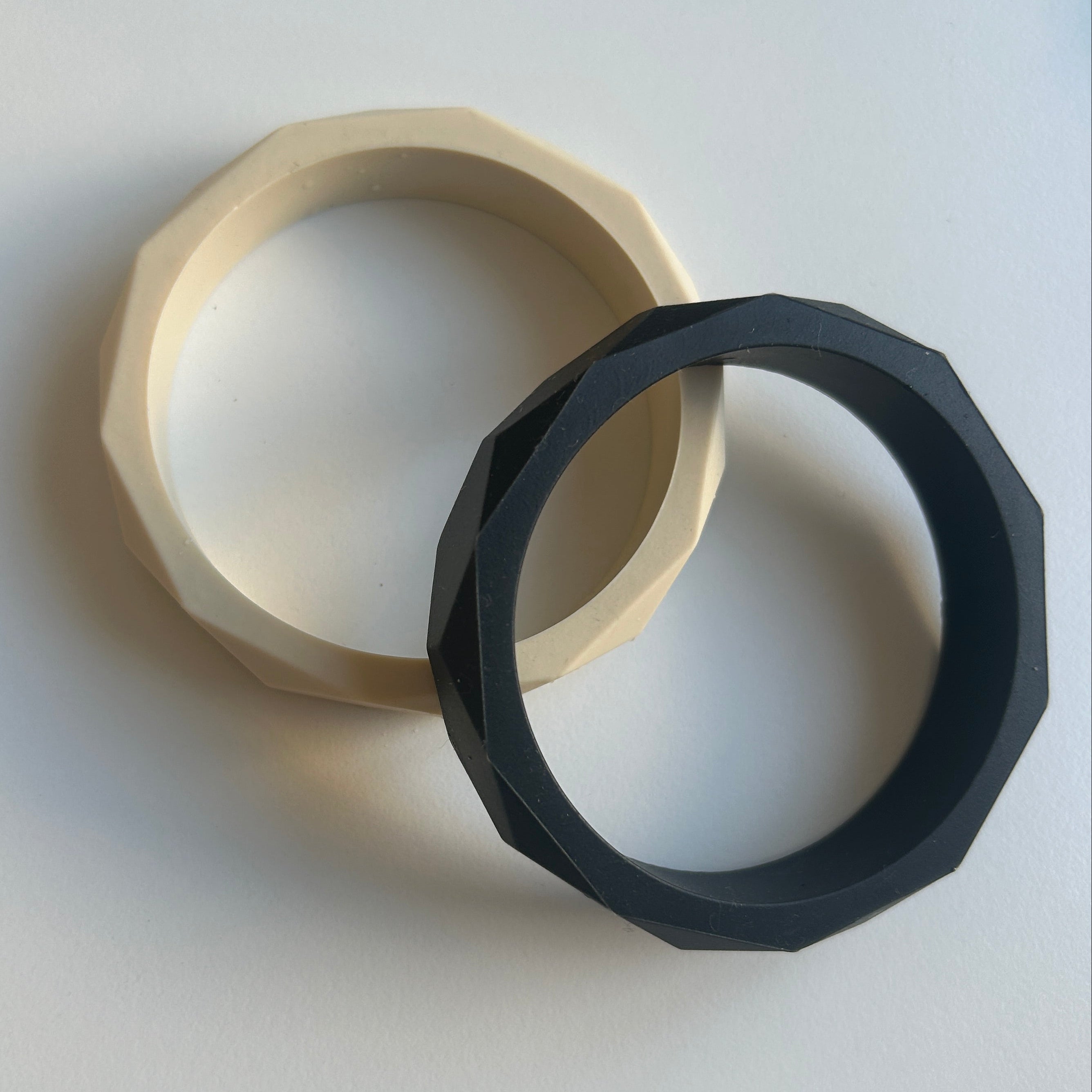 Two silicone braceles, one black and one beige, on a white background.